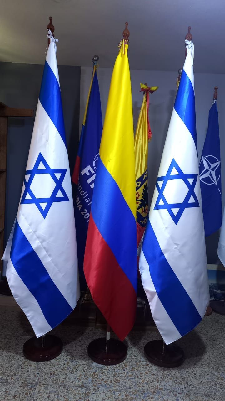 Flags of Israel, Colombia, and NATO displayed on stands indoors.