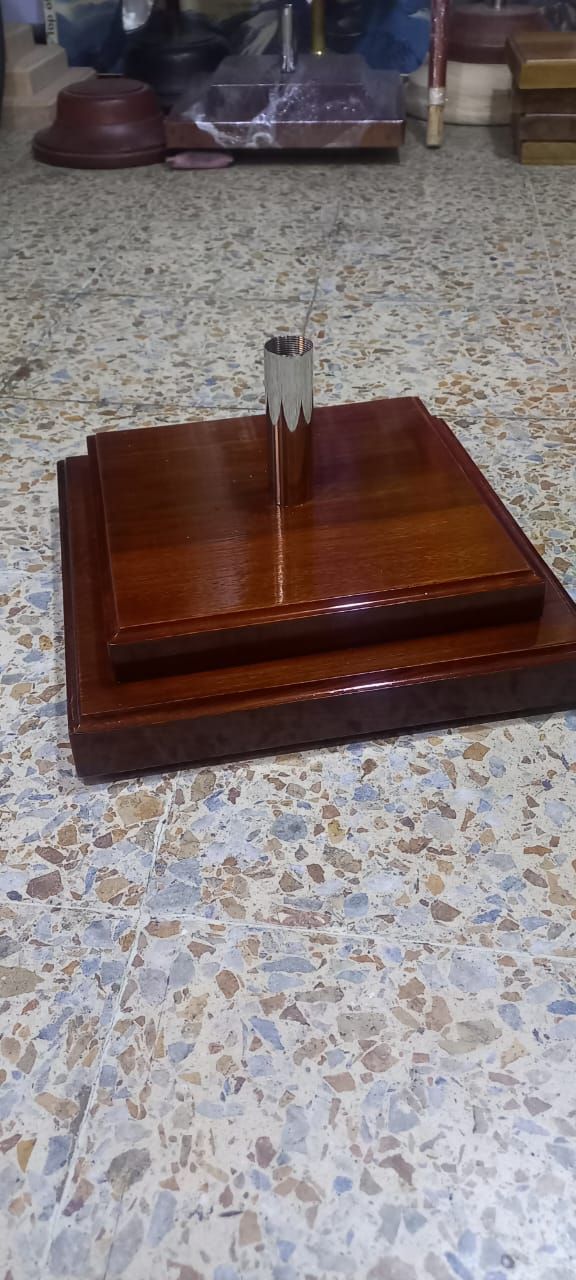 Base cuadrada de madera con un pequeño poste de metal sobre una encimera moteada.