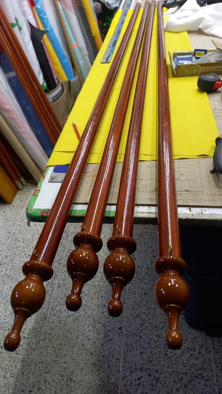 Cuatro barras de cortina de madera con remates torneados sobre una mesa de trabajo amarilla en un taller.