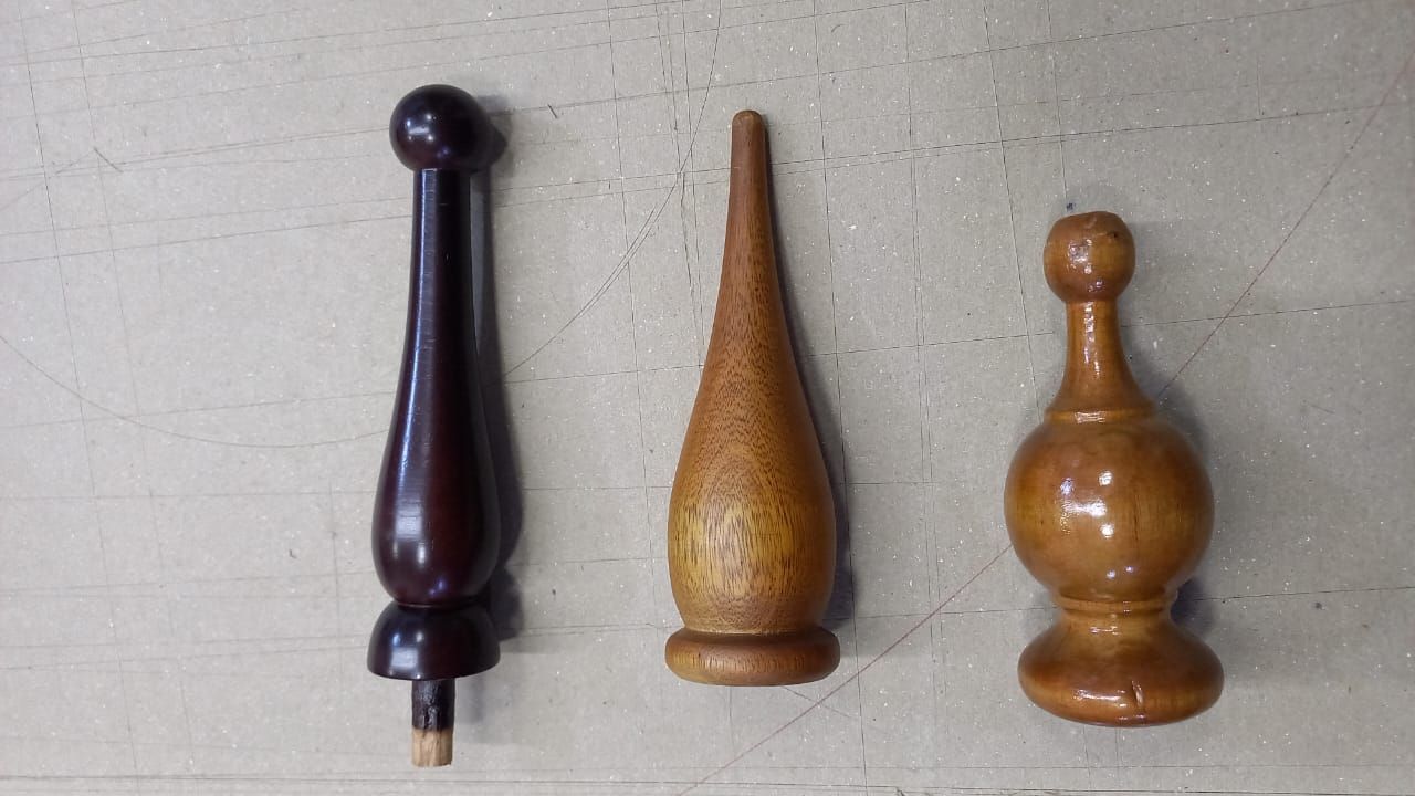 Tres pequeños pomos o remates de madera torneada en marrón oscuro, tostado y marrón claro sobre una superficie gris.