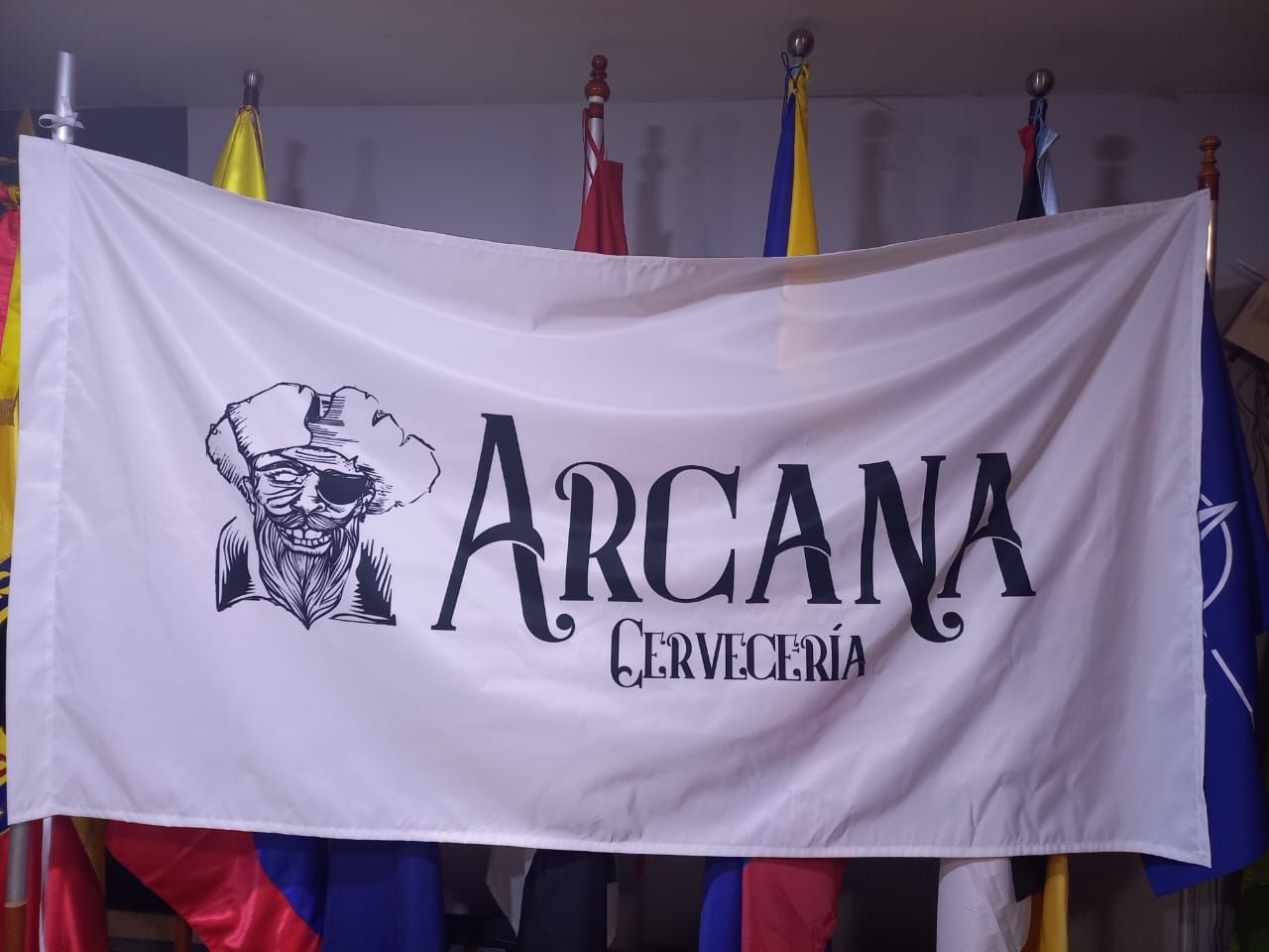 Pancarta blanca con la palabra “ARCANA” y la ilustración de una calavera, colgada en el interior.