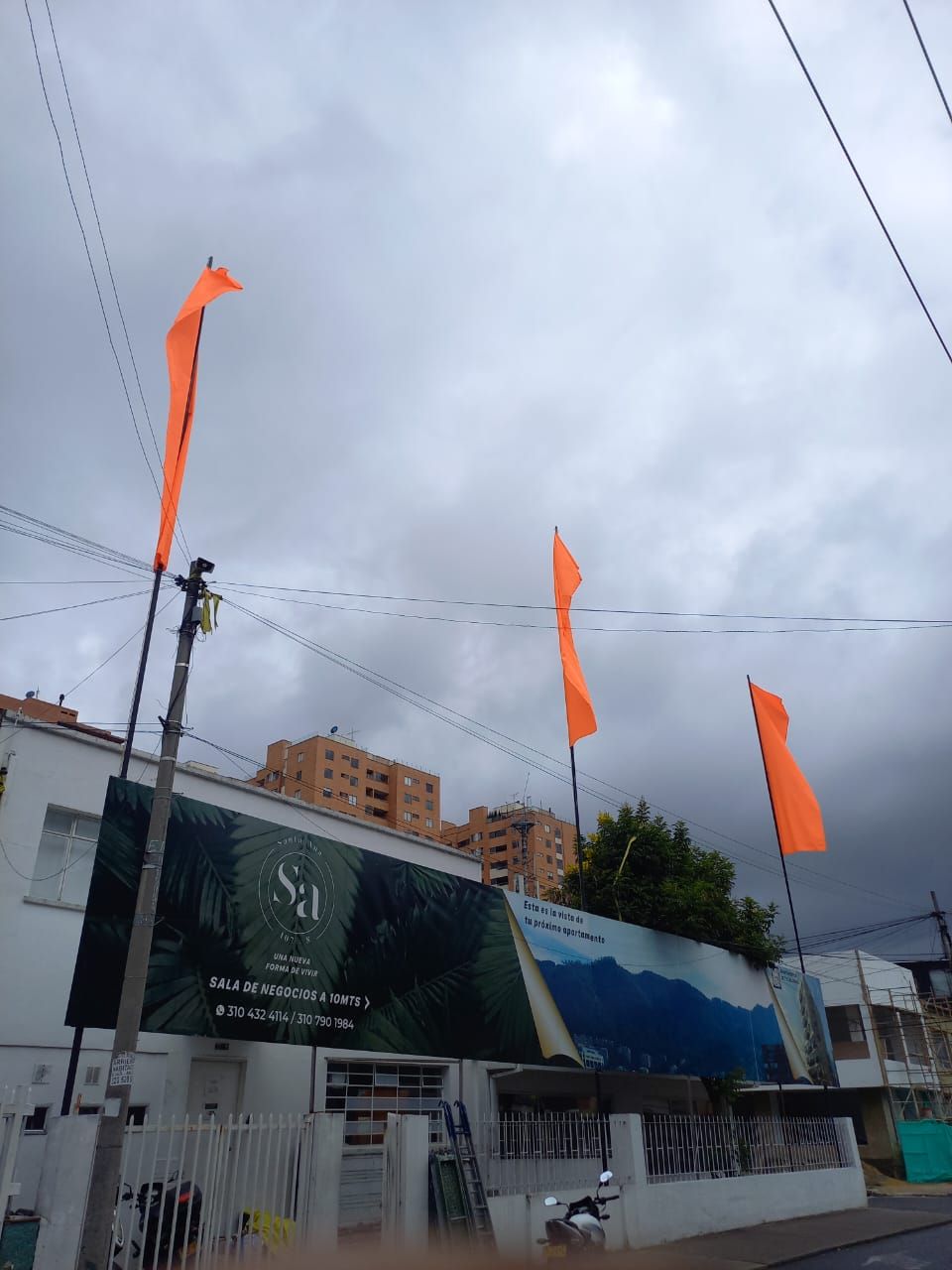 Escena callejera con banderas naranjas sobre un edificio y cielo nublado.