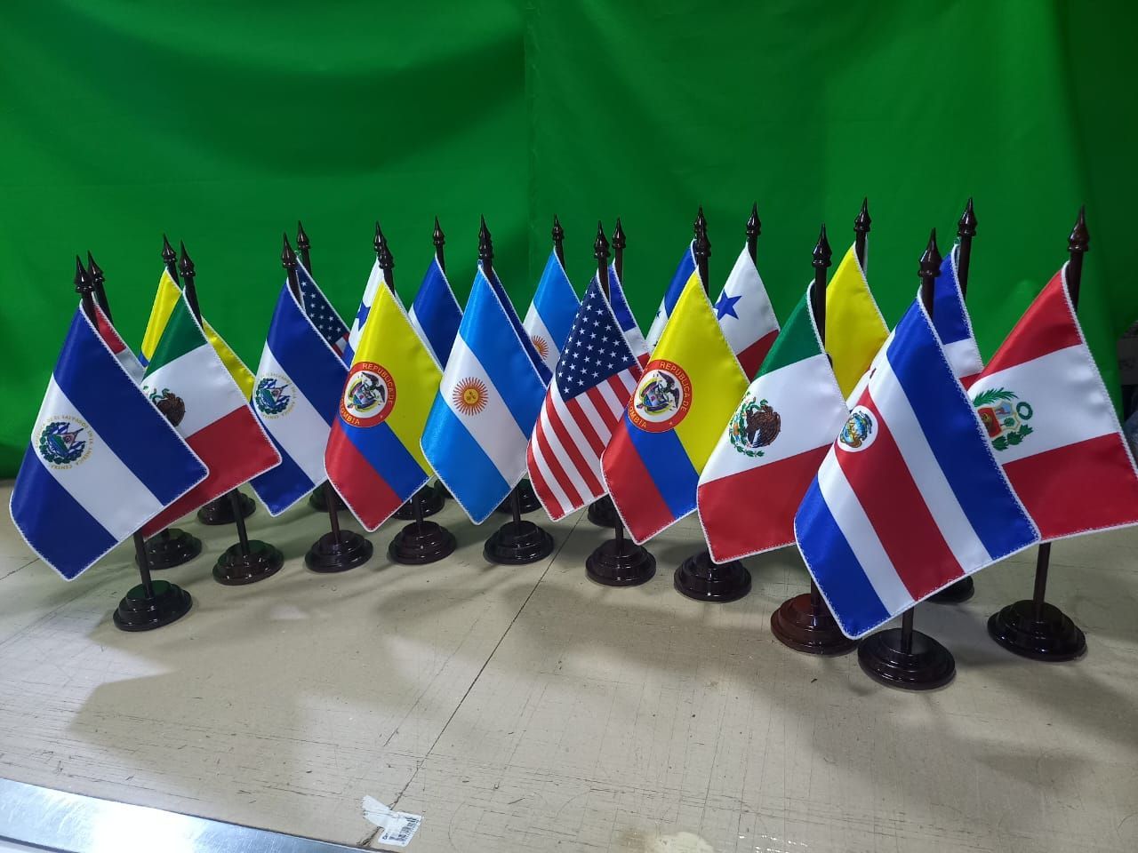 Hilera de pequeñas banderas de escritorio de varios países sobre soportes negros contra un fondo verde.