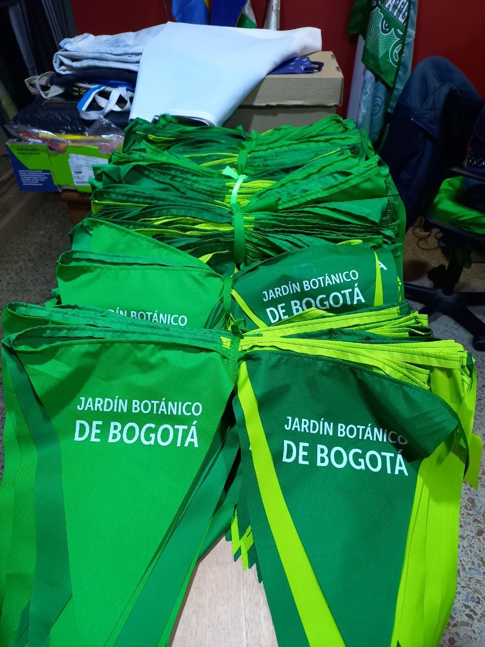 Bolsas de tela verdes del Jardín Botánico de Bogotá apiladas en el interior sobre una mesa.