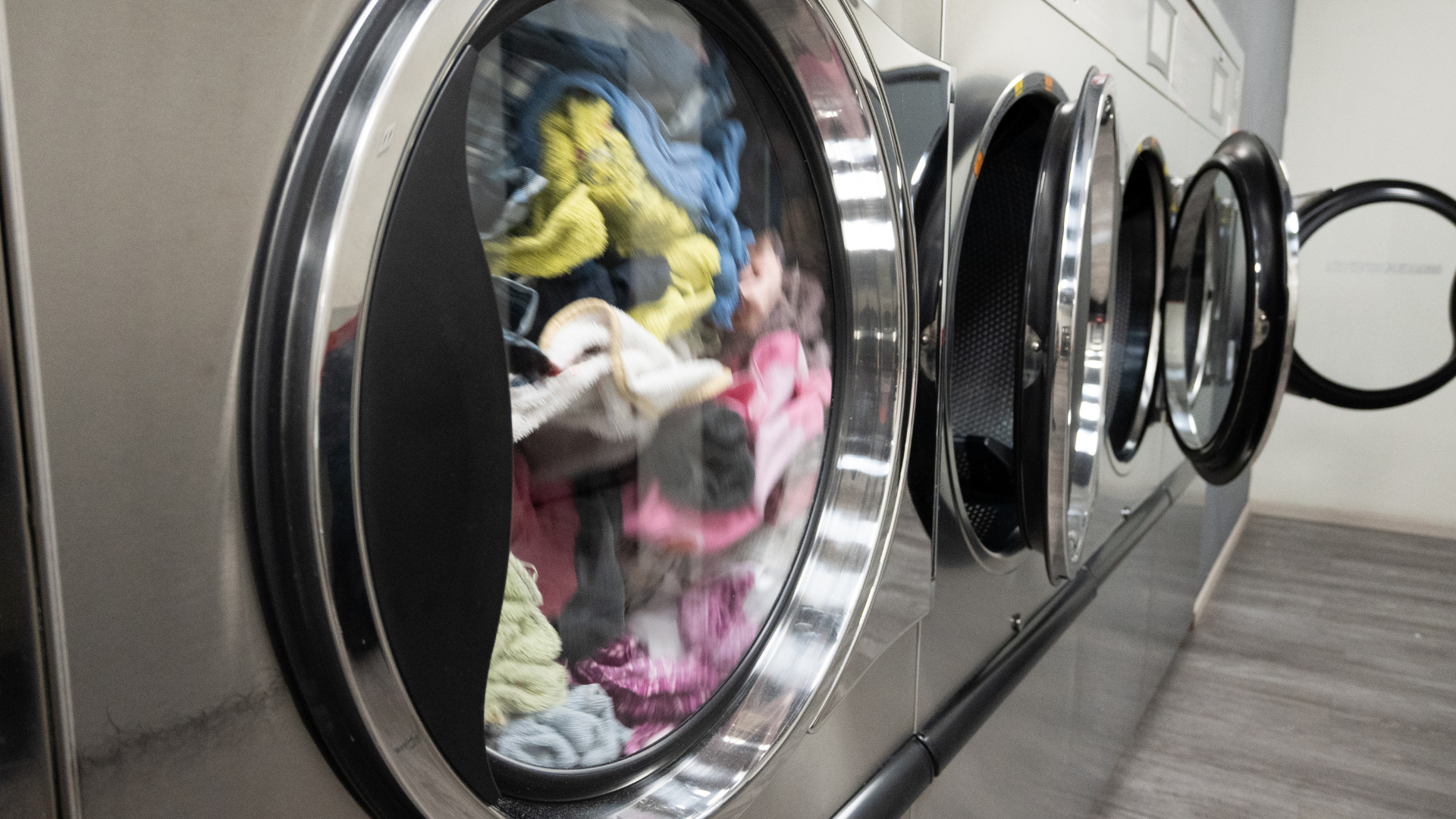 Row of commercial washing machines, one filled with colorful clothing.