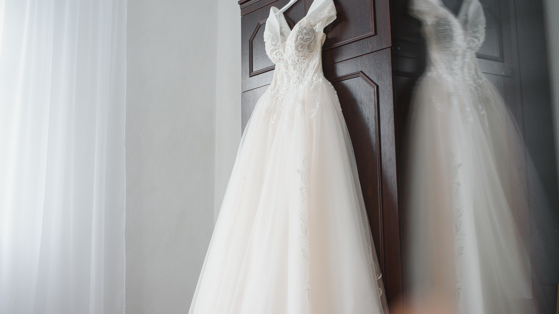 Wedding dress hanging on a dark wooden door with its reflection visible.