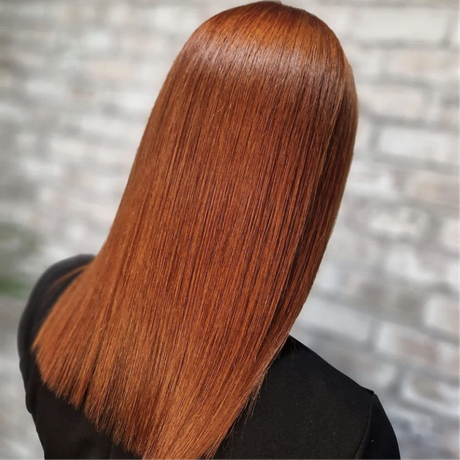 Straight copper-red hair seen from behind against a blurred brick wall.