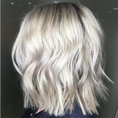 Short wavy platinum blonde bob haircut with darker roots against a dark background