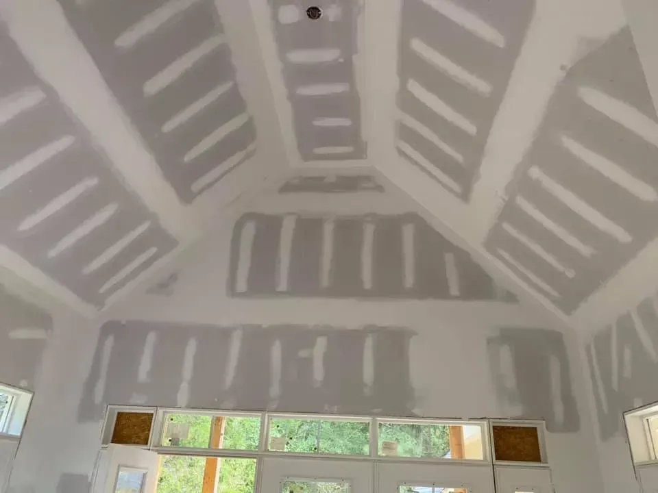 Interior with unfinished drywall ceiling and walls, exposed joint patches, and a window at the bottom.