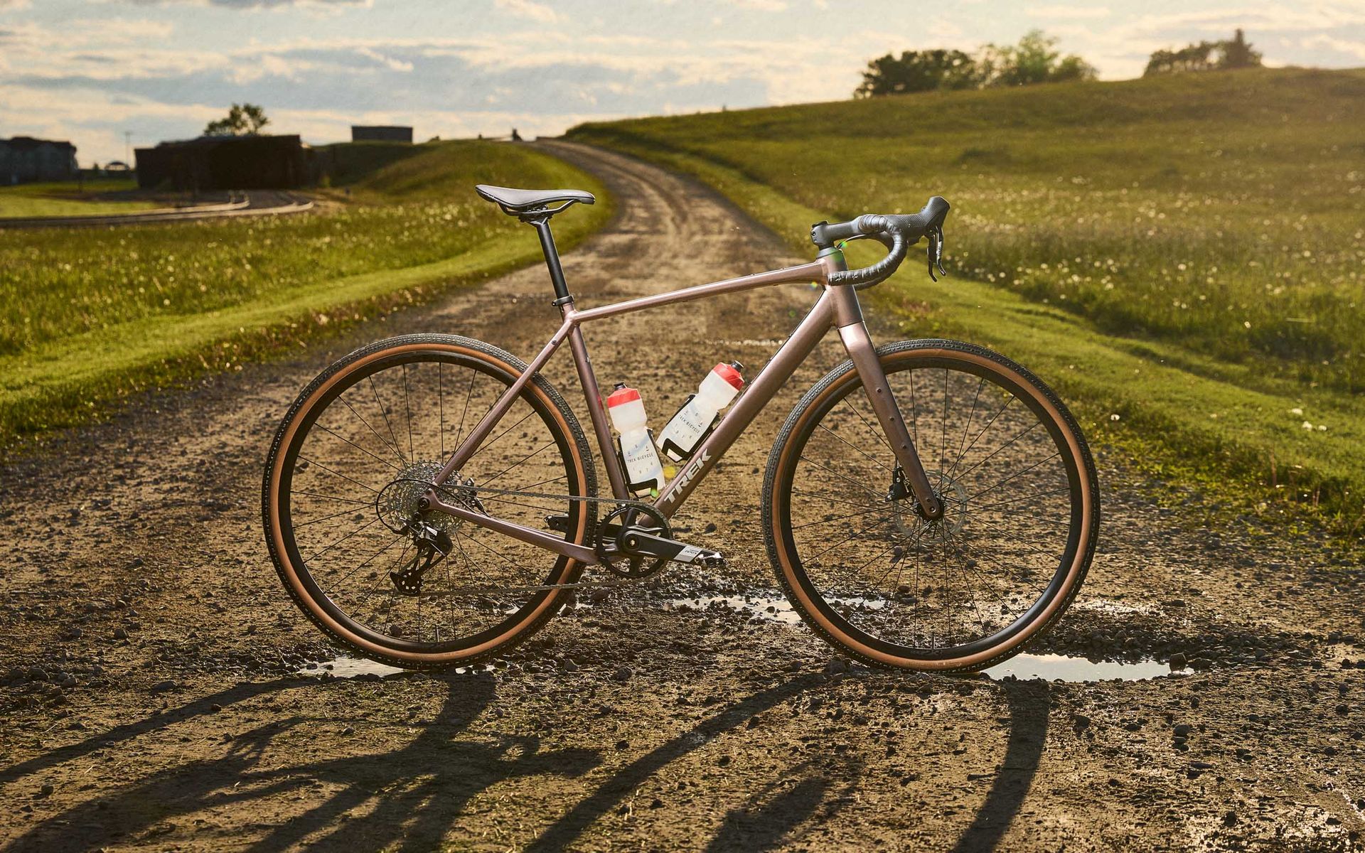 Vélo de route sur un chemin de gravier bordant des champs verdoyants sous un ciel nuageux.
