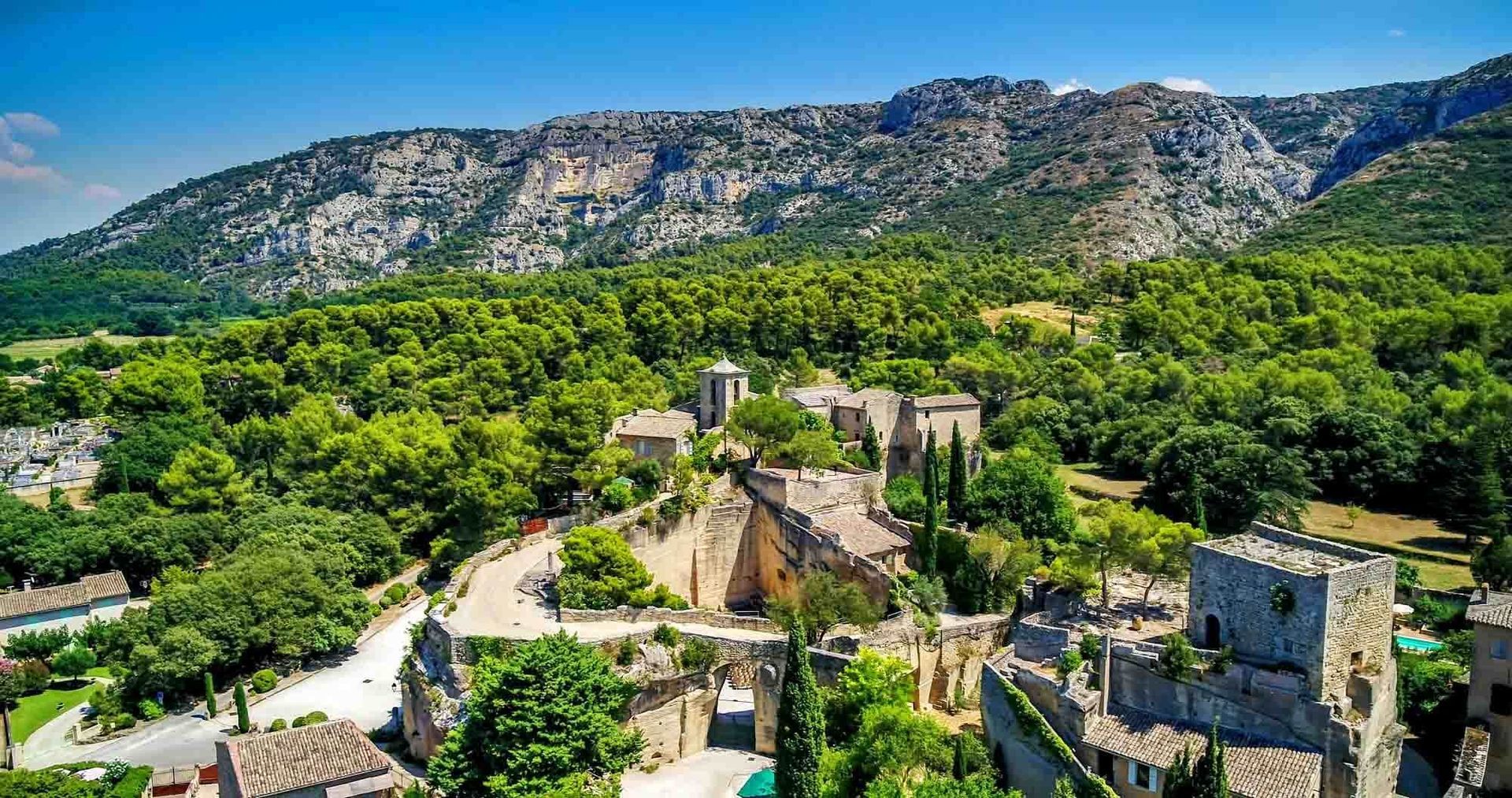Ruines de pierre dans une vallée verdoyante, avec une montagne rocheuse en toile de fond, sous un ciel d'un bleu limpide.