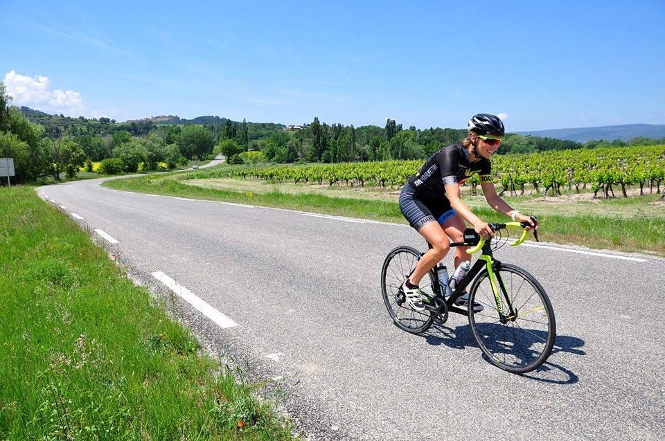 Cycliste roulant sur une route de campagne bordée de champs verdoyants sous un ciel d'un bleu éclatant