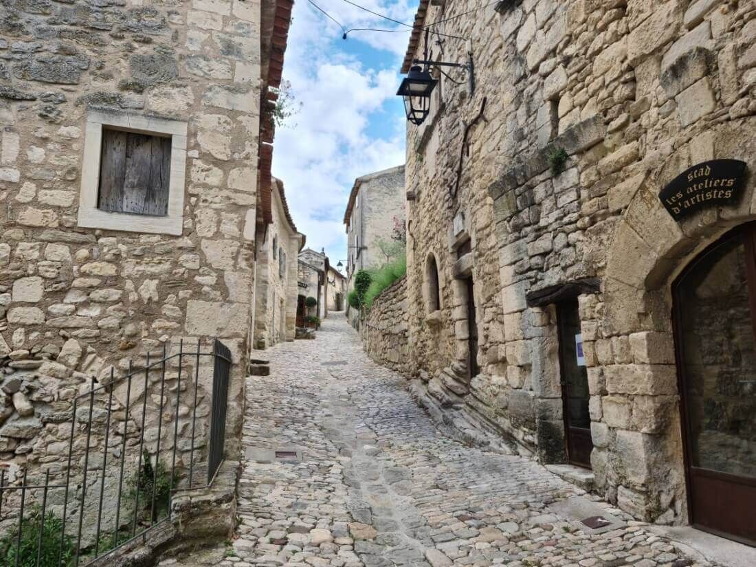 Une ruelle pavée étroite bordée de vieux bâtiments en pierre et un lampadaire sous un ciel bleu