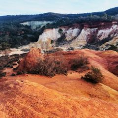 Falaises orangées érodées au pied d'une colline boisée sous un ciel nuageux