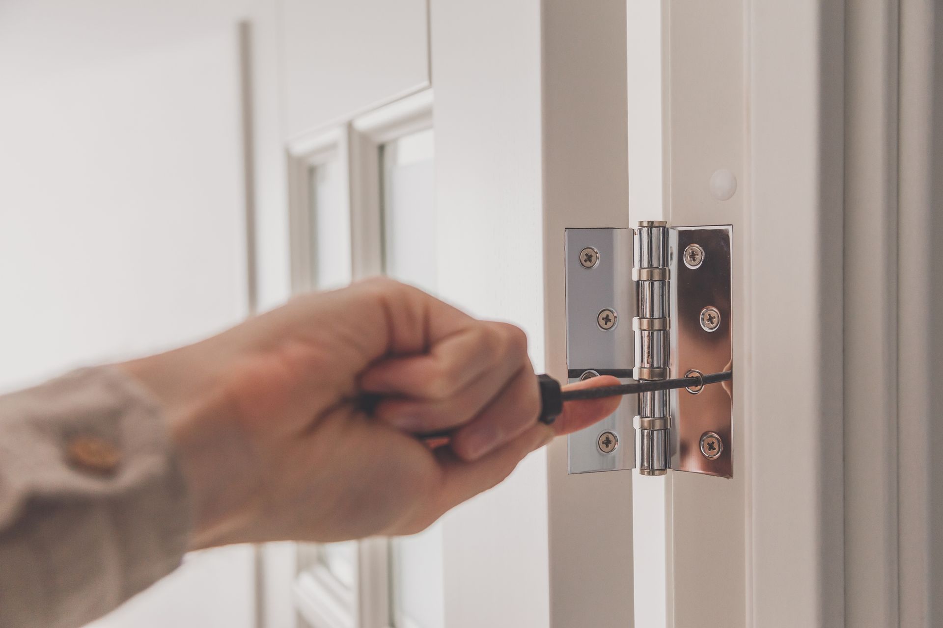 Hand tightening a screw on a silver door hinge with a screwdriver