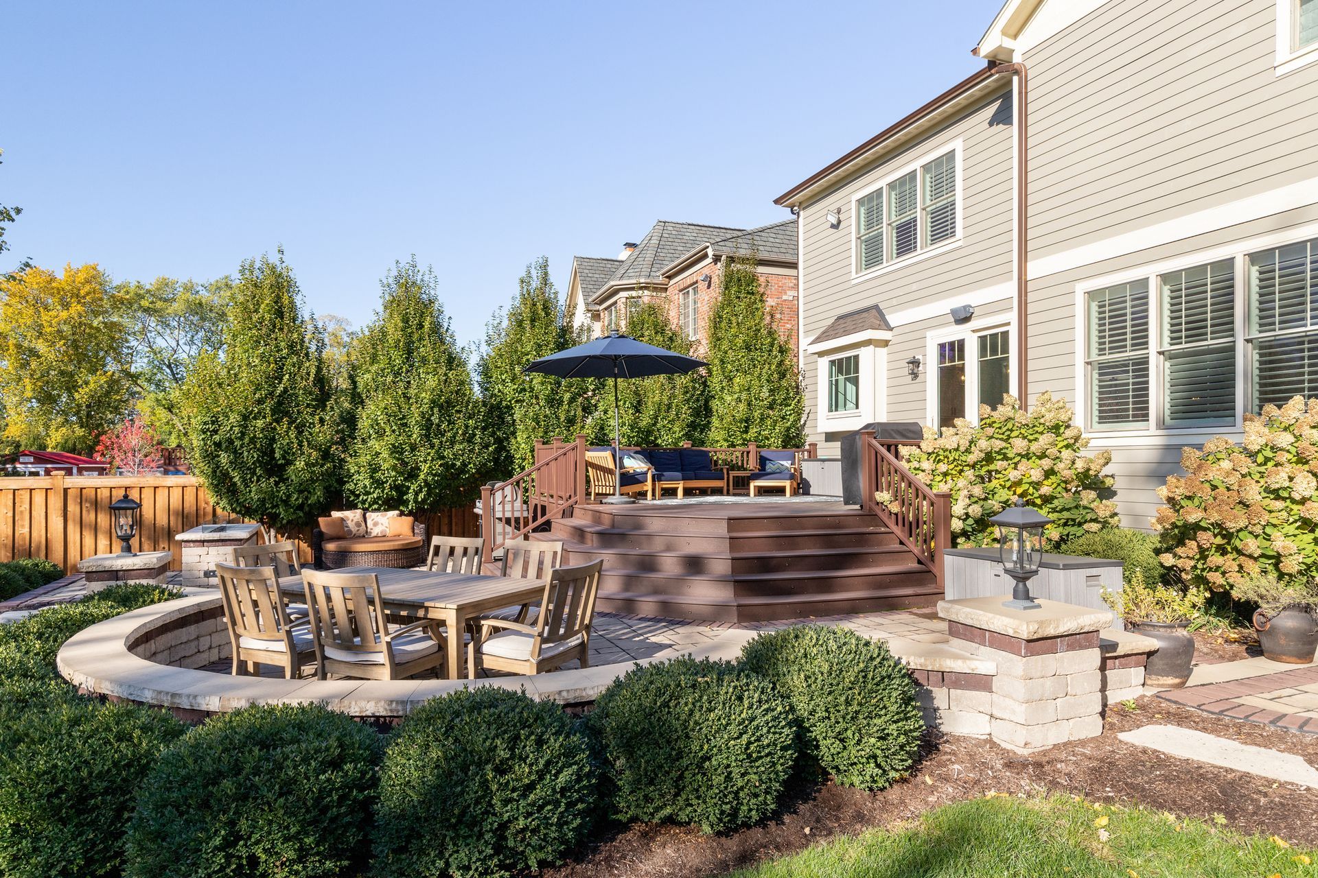 Backyard patio with outdoor dining set, lounge chairs, umbrella, and landscaped garden beside a house