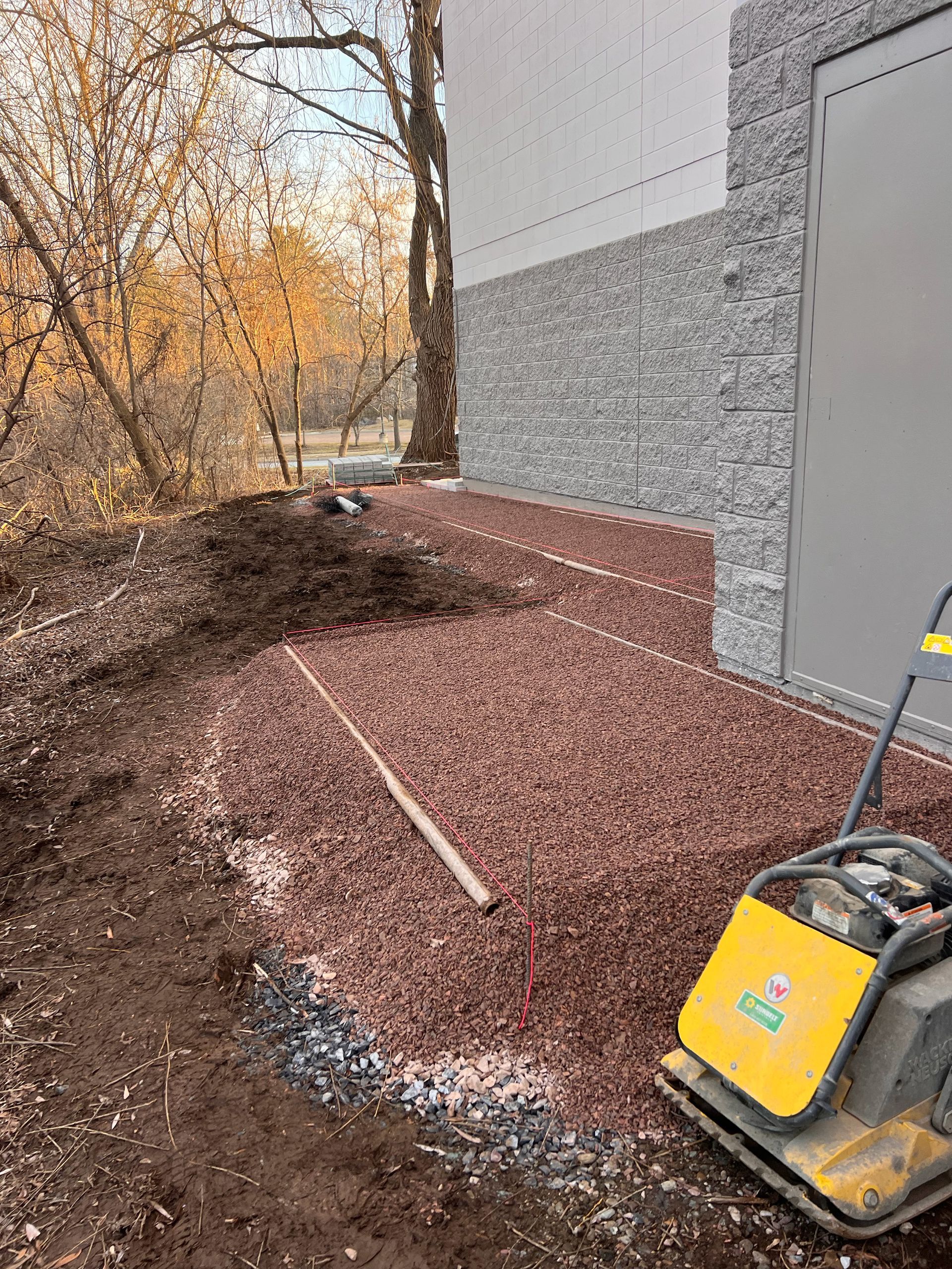 Construction work area with gravel spread beside a building and a yellow compactor on the right