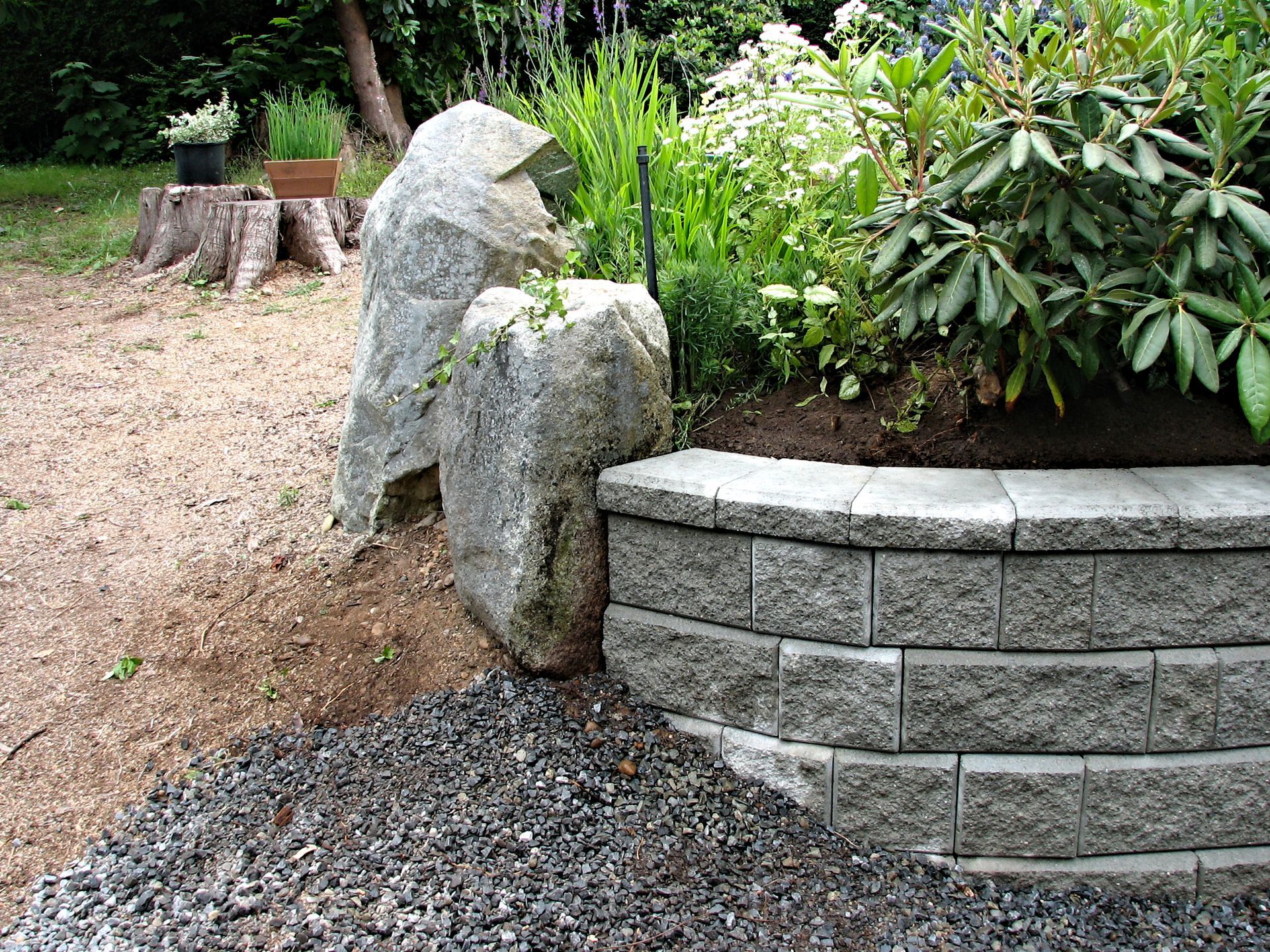 Stone sculpture beside a curved gray retaining wall in a landscaped garden path
