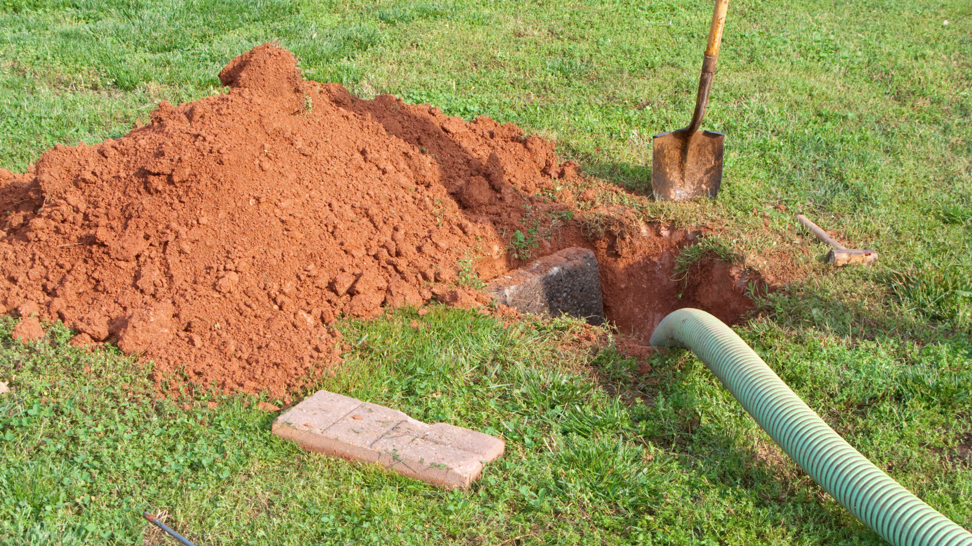 Sewer vacuum truck clearing a clogged pipe, with a green hose leading into a hole in the ground.