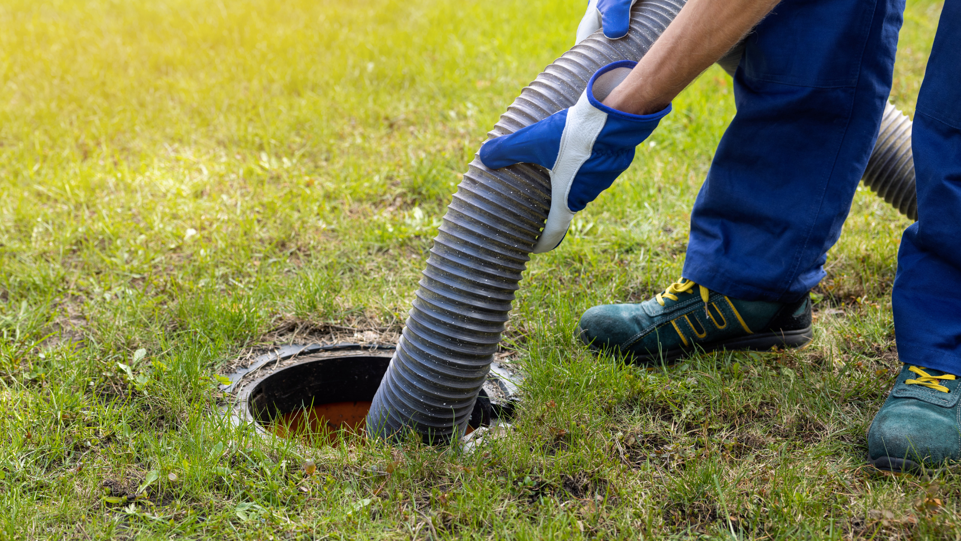 Worker in blue gloves inserts a corrugated hose into a round ground opening on grass.