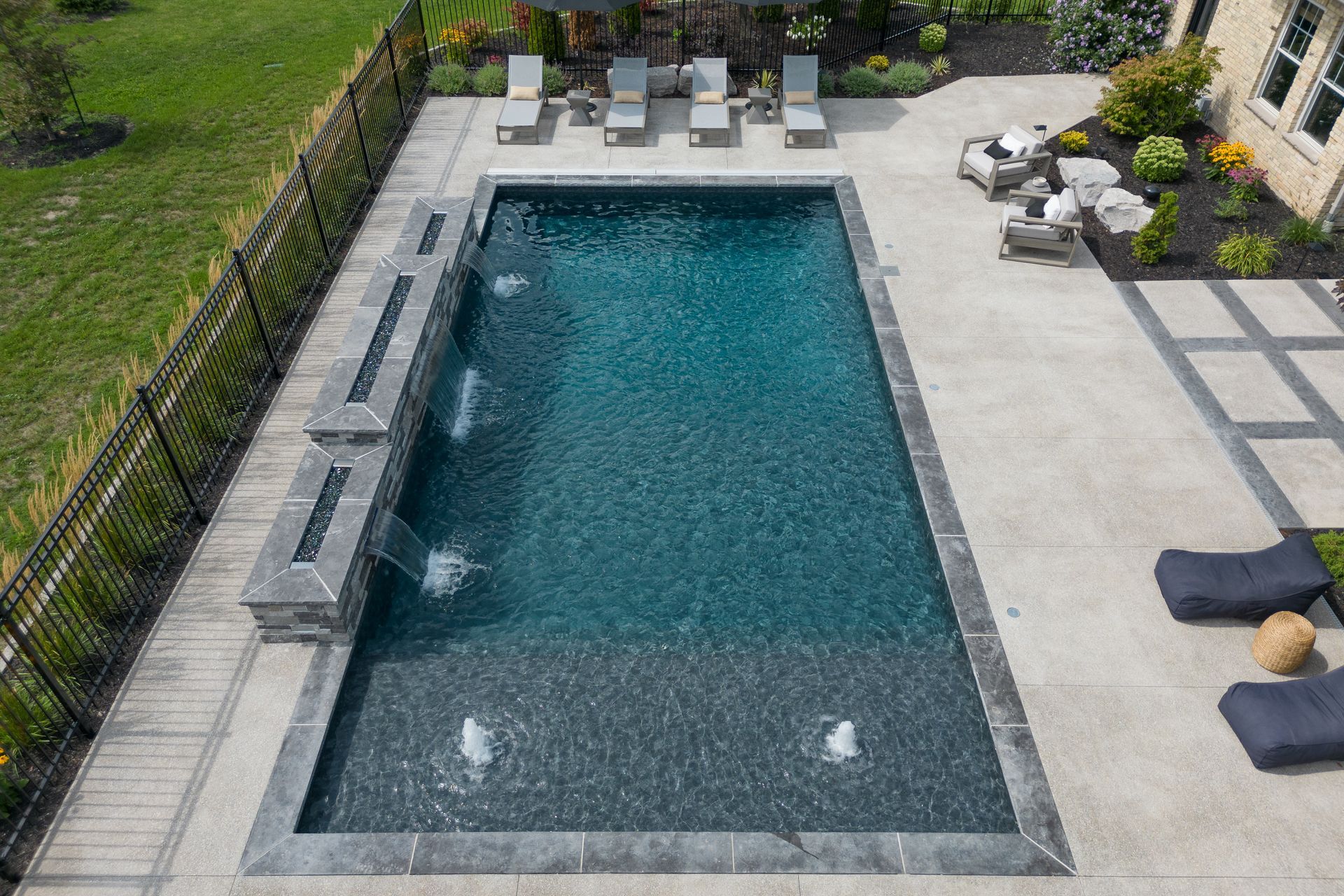 Rectangular backyard swimming pool with lounge chairs and stone patio surrounding it