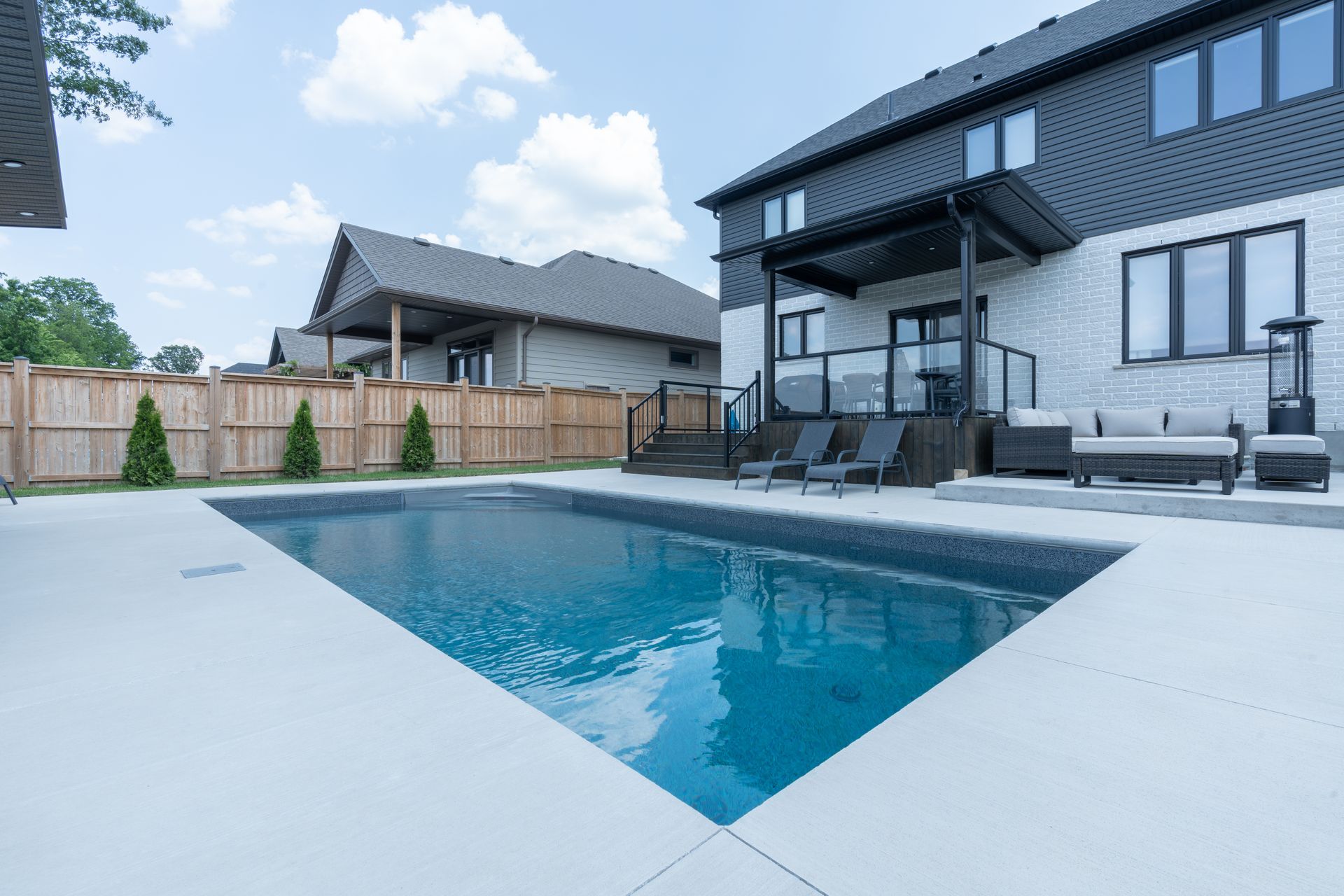 Modern home patio with a rectangular swimming pool and lounge chairs under a cloudy sky
