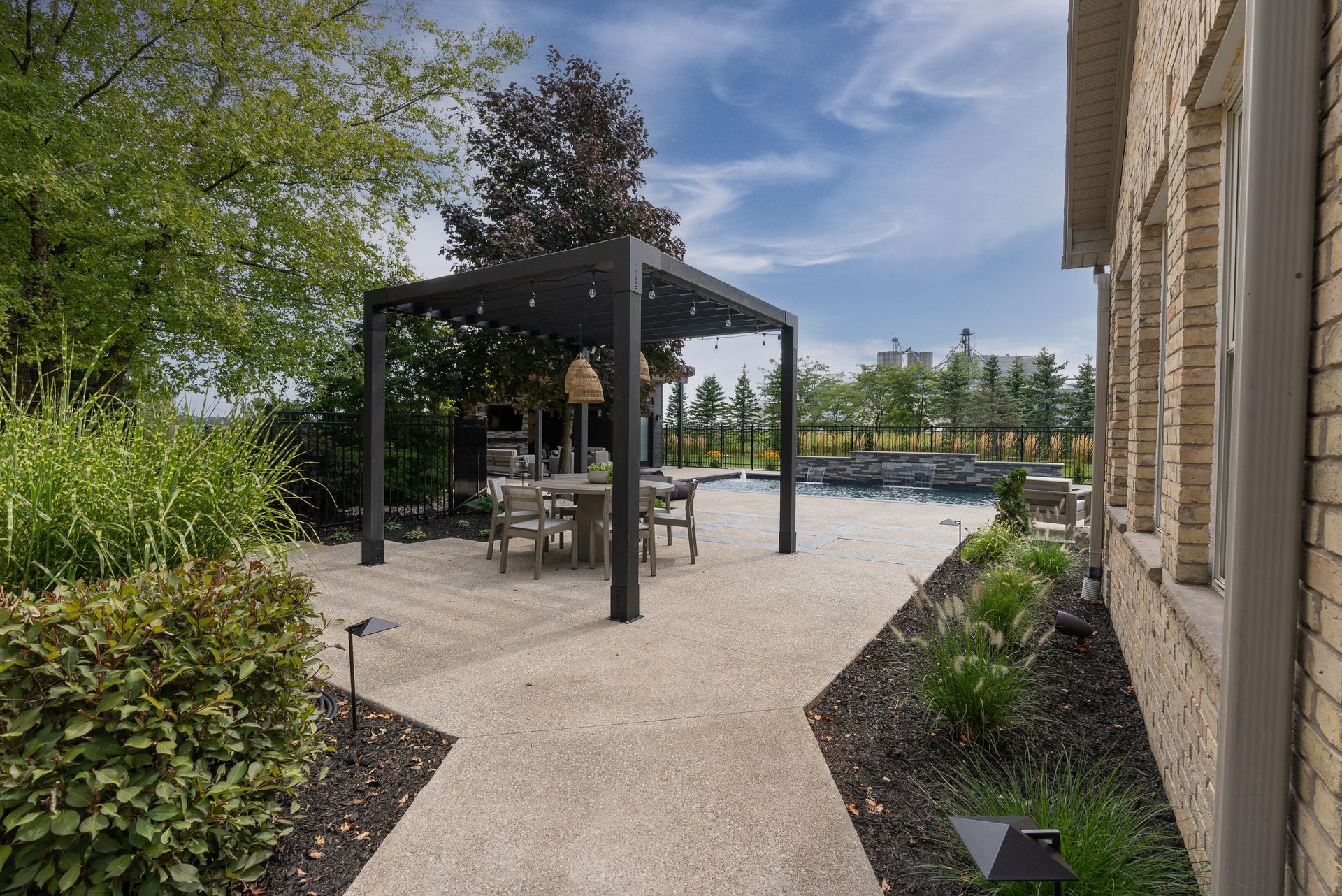 Backyard patio with a black pergola, dining table, and landscaped garden beside a house