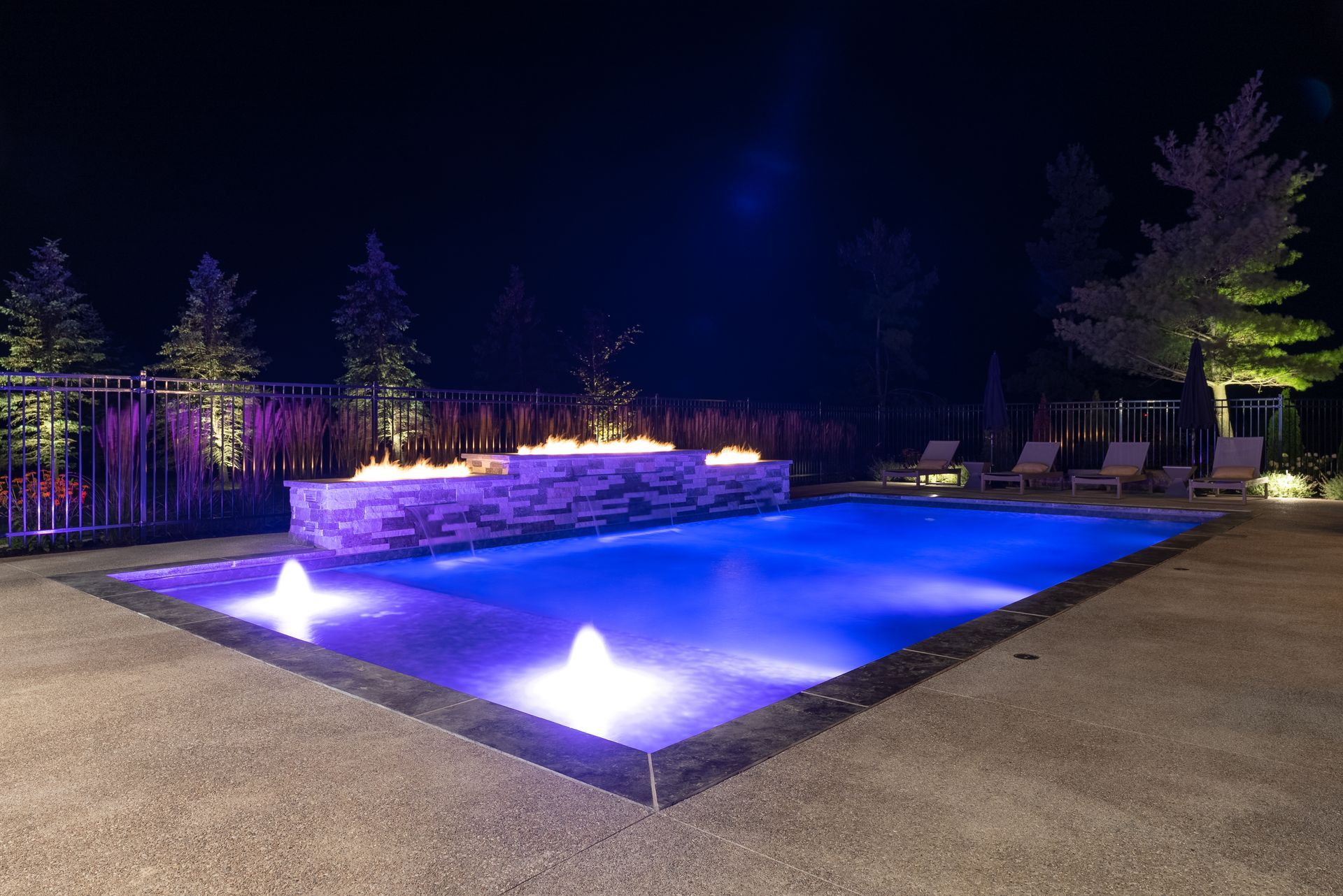 Illuminated backyard pool at night with blue water and glowing fountain lights