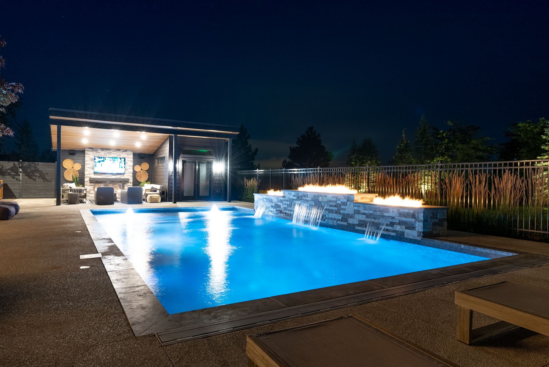 Night-lit backyard pool beside a modern patio and outdoor lounge area