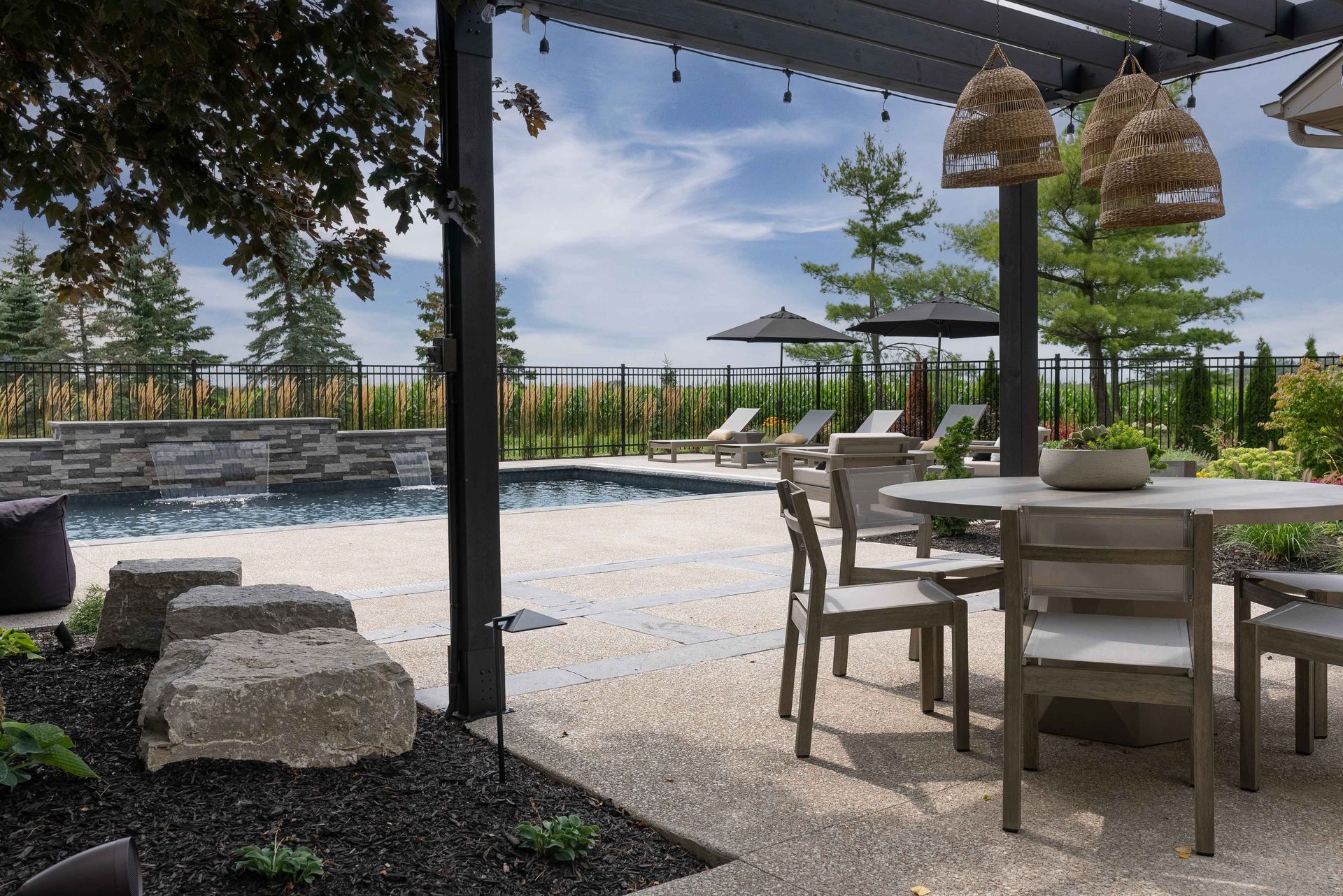 Patio dining area with wooden table and chairs overlooking a pool and landscaped garden
