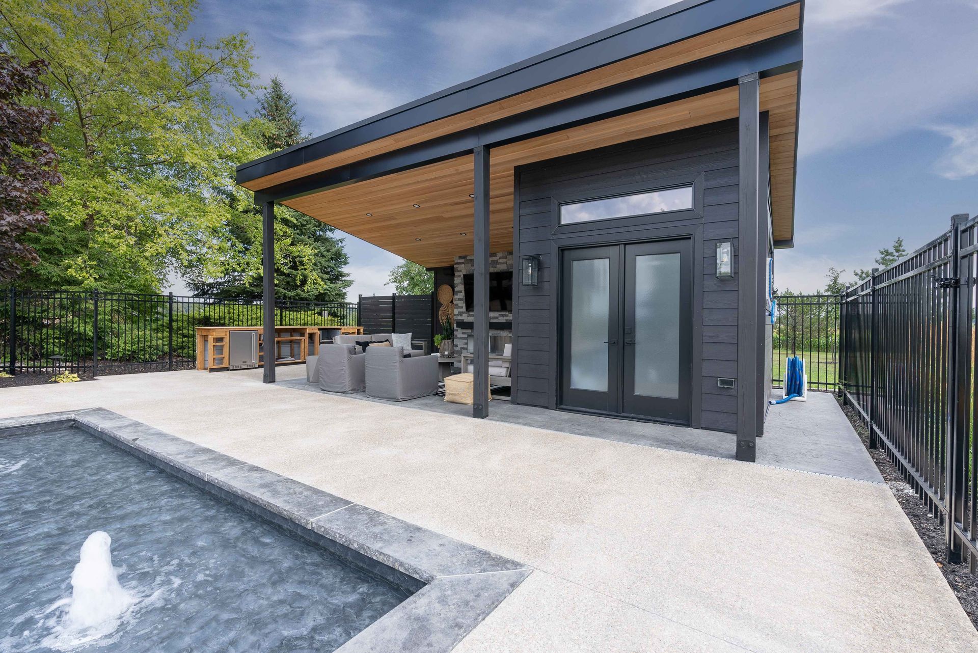 Modern outdoor pool area with a covered patio, gray stone facade, and glass doors