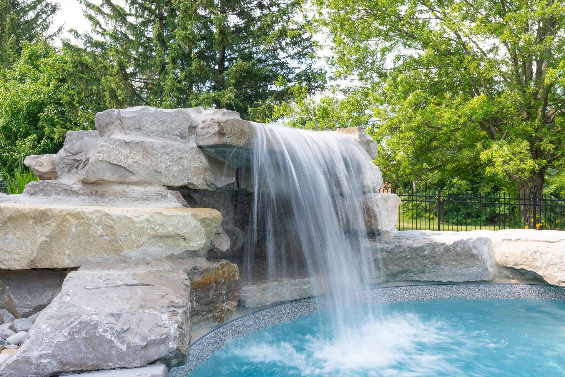 Artificial waterfall cascading into a blue pool beside stacked stone and green trees