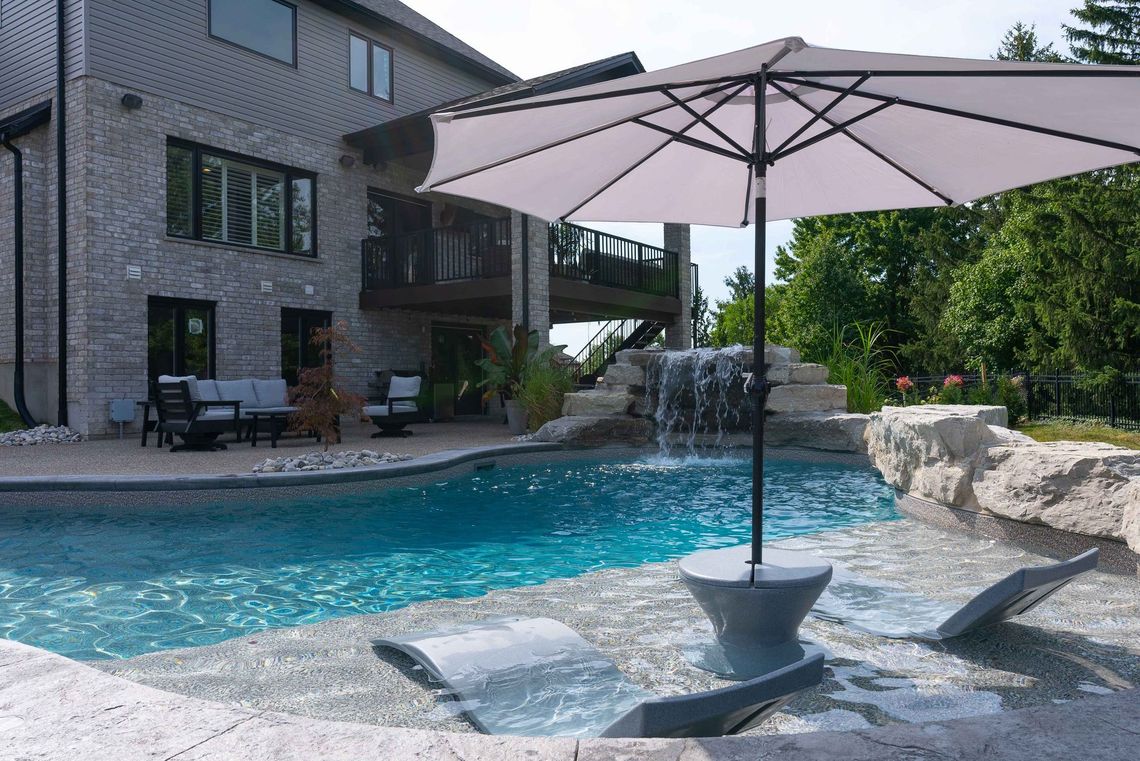 Backyard patio with a swimming pool, lounge chairs, and a large umbrella beside a modern house