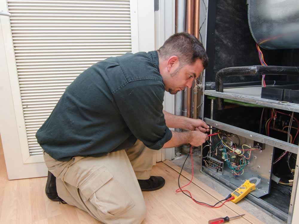 Man kneeling, using multimeter to troubleshoot HVAC system in an indoor setting.