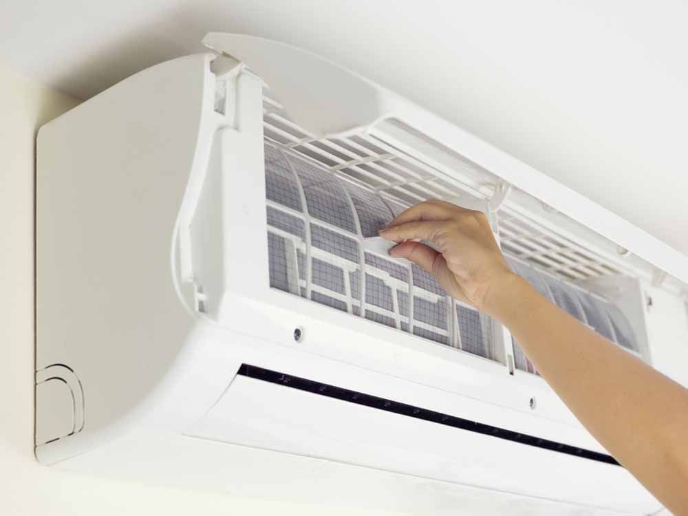 A person's hand removing an air filter from a white wall-mounted air conditioner.