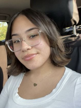 Young woman with glasses and a white top smiles.