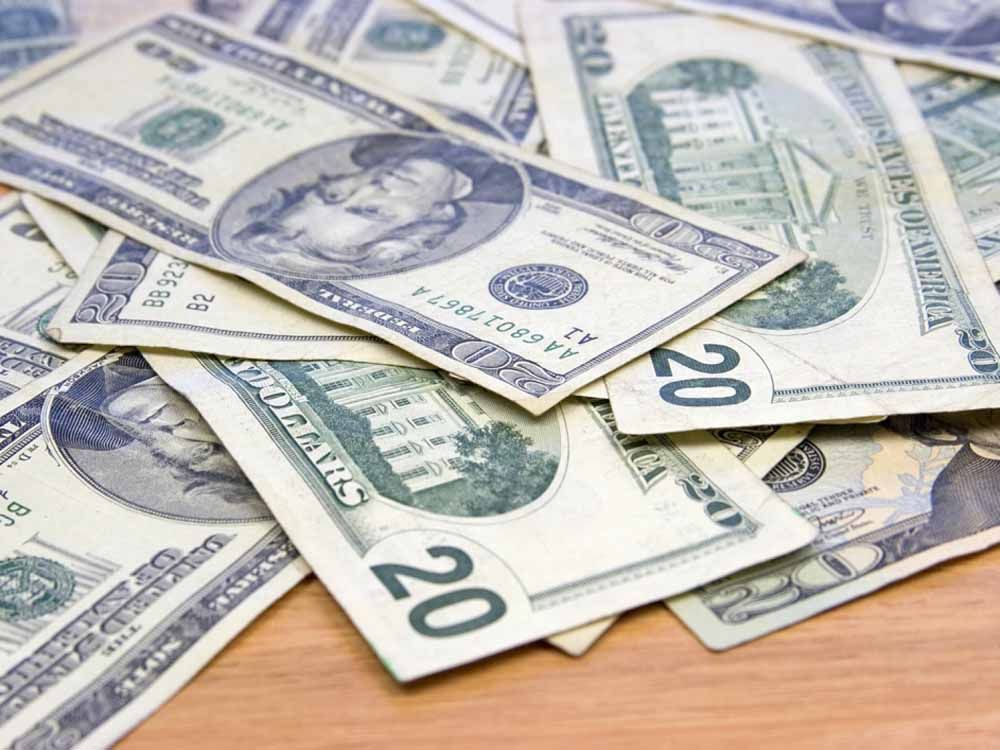 Pile of twenty-dollar bills scattered on a wooden surface.