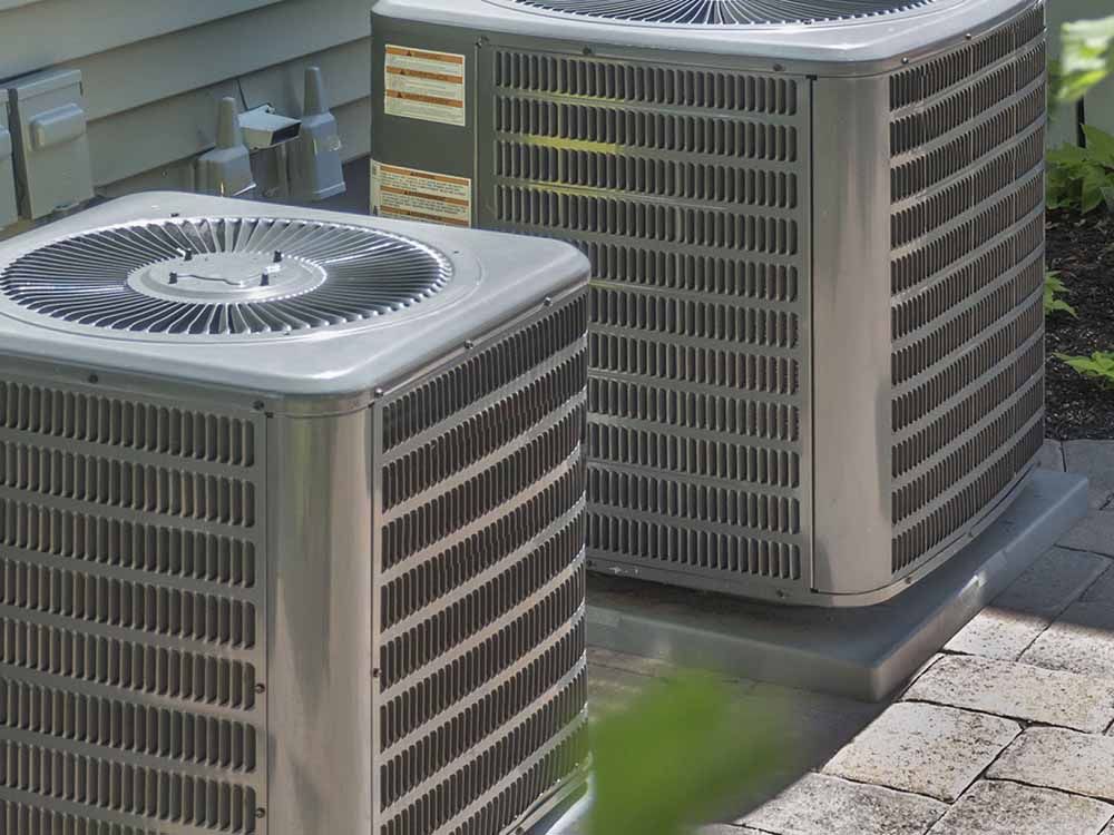 Two silver AC units side-by-side outside a house on a patio.