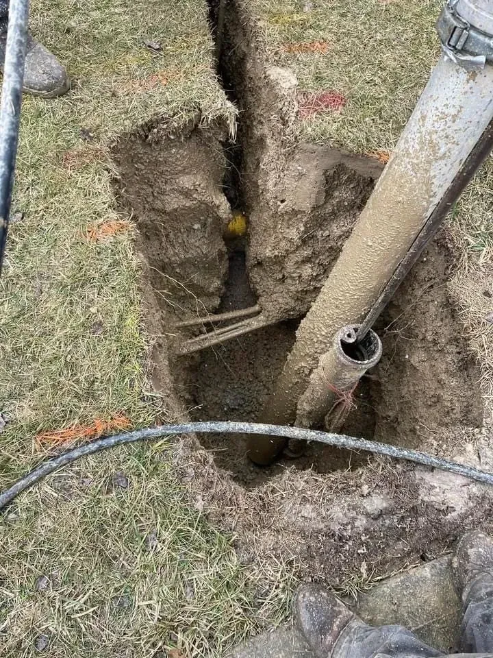 Trench in grass with pipe, dirt and a yellow marker sphere, possibly construction or utility work.