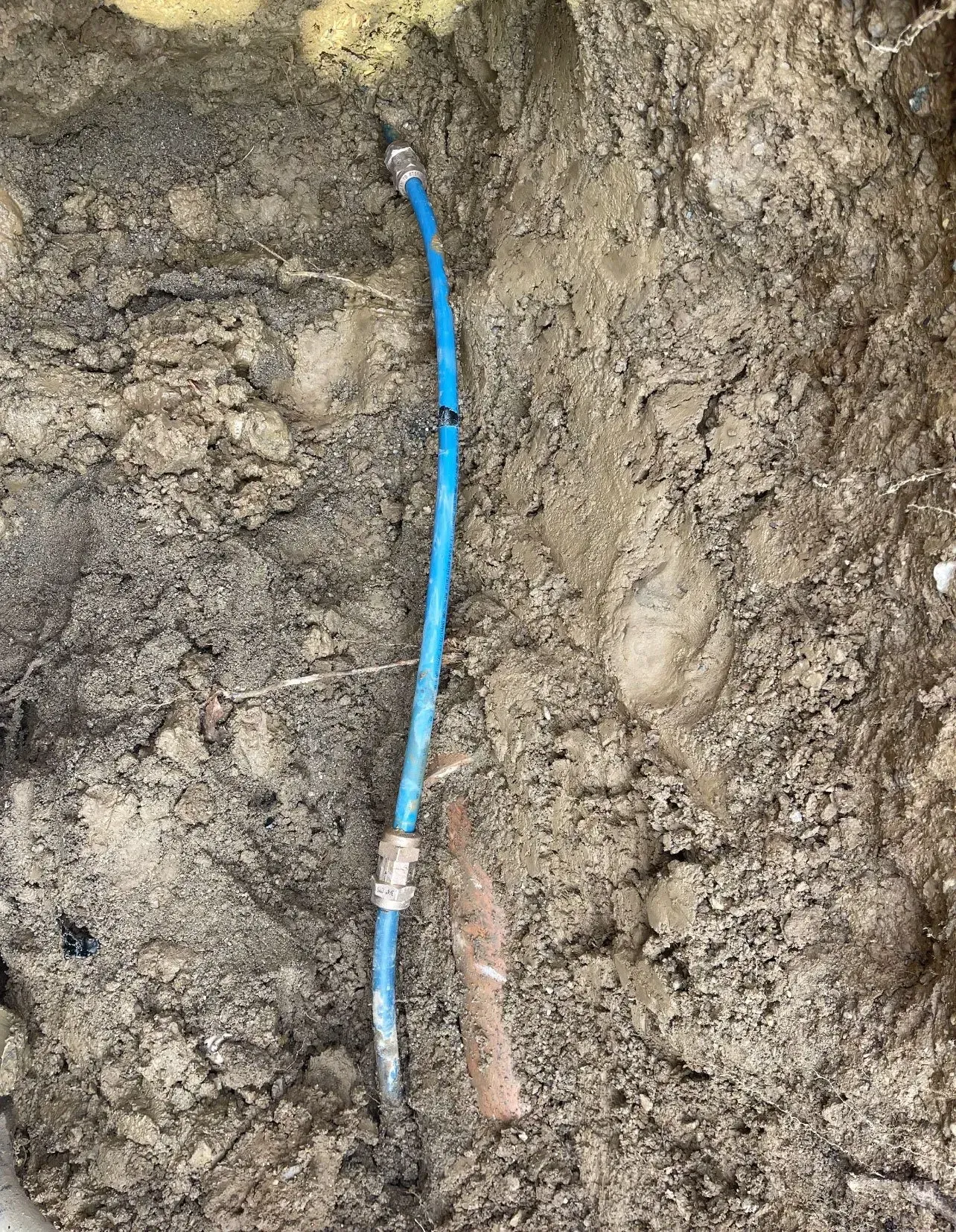 Blue water pipe partially buried in dirt, with fittings.