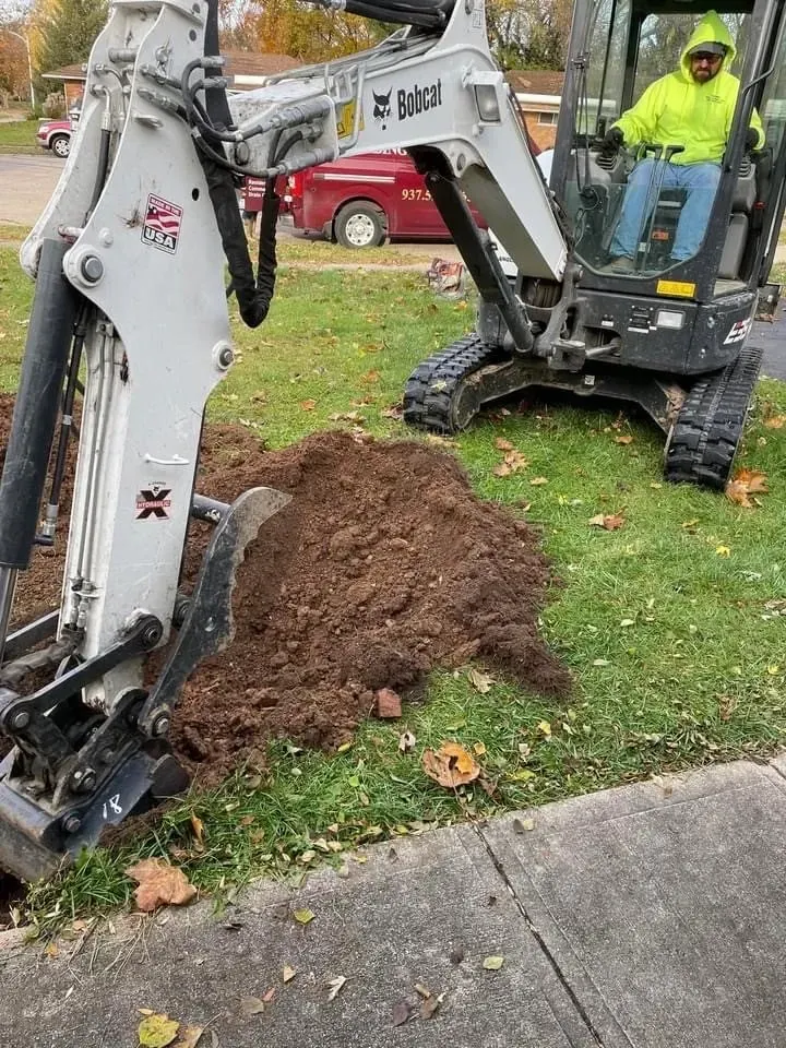 Bobcat excavator digging in a yard; operator in yellow vest.