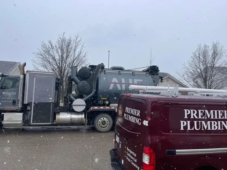 Premier Plumbing truck and large vacuum truck parked on a snowy street.