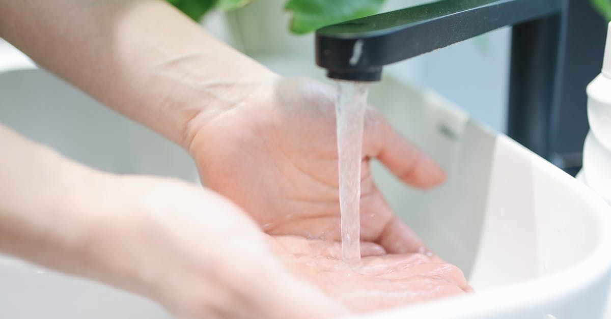 Hands being washed under a running faucet in a white sink.