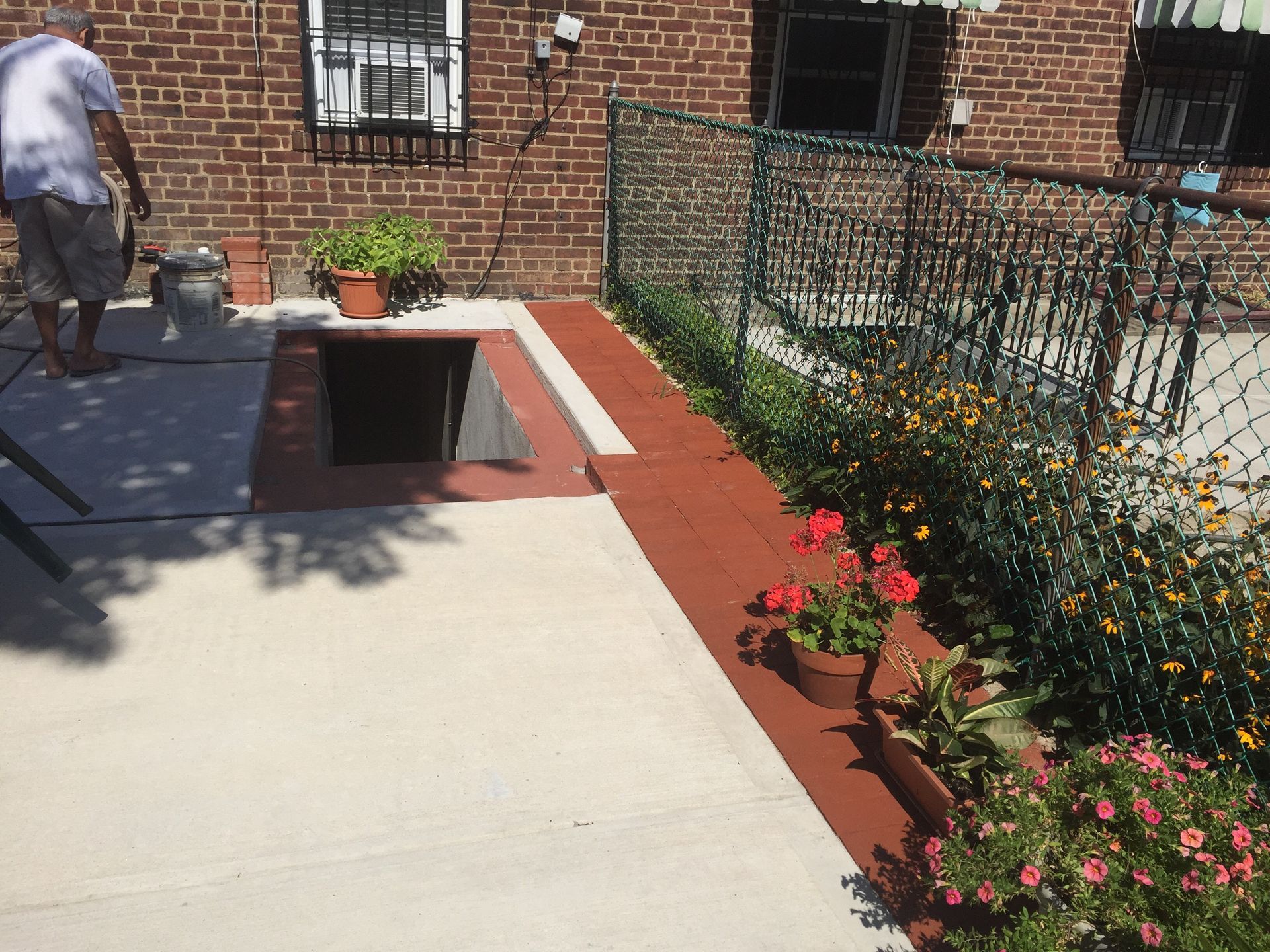 Patio with a red planter, flowers, brick wall, and a person walking at left