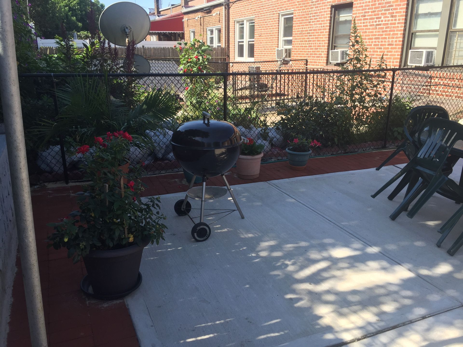 Patio with a charcoal grill, potted flowers, and black chairs beside a brick wall and fence