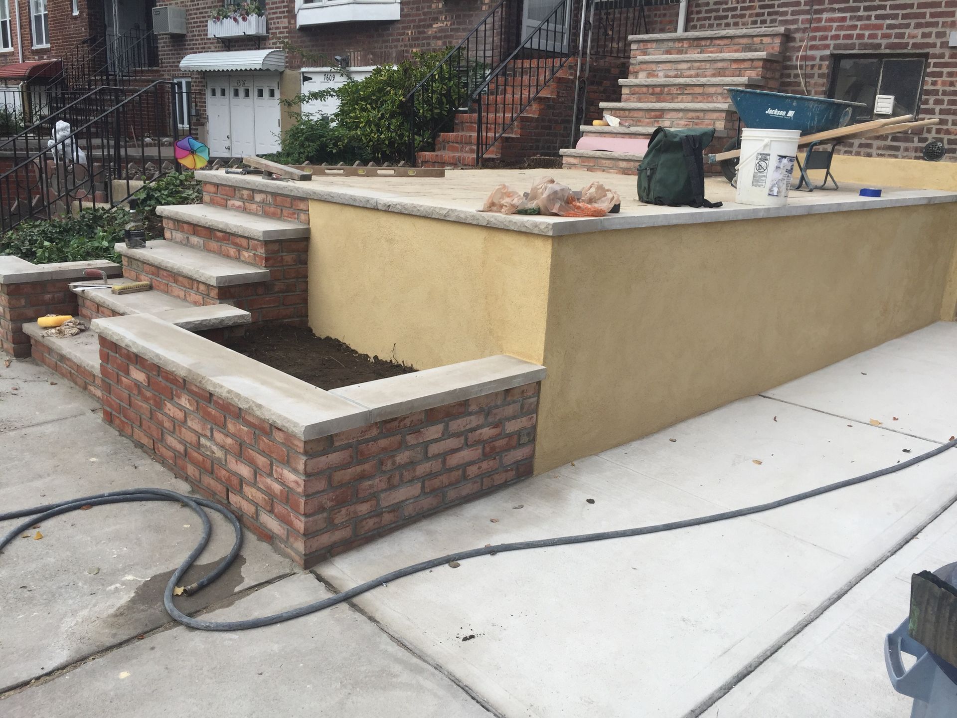Brick steps and raised planter wall beside a concrete driveway in a front yard