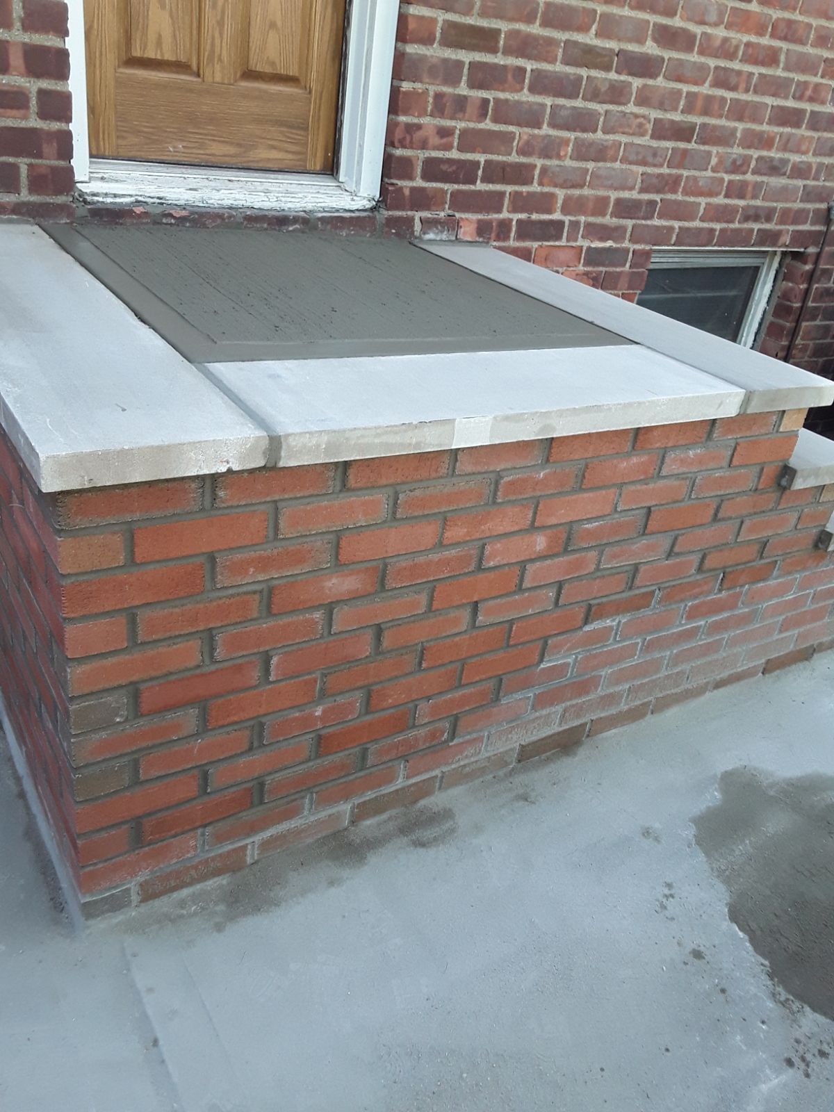 Brick front porch with a concrete step, white trim, and a boarded door.