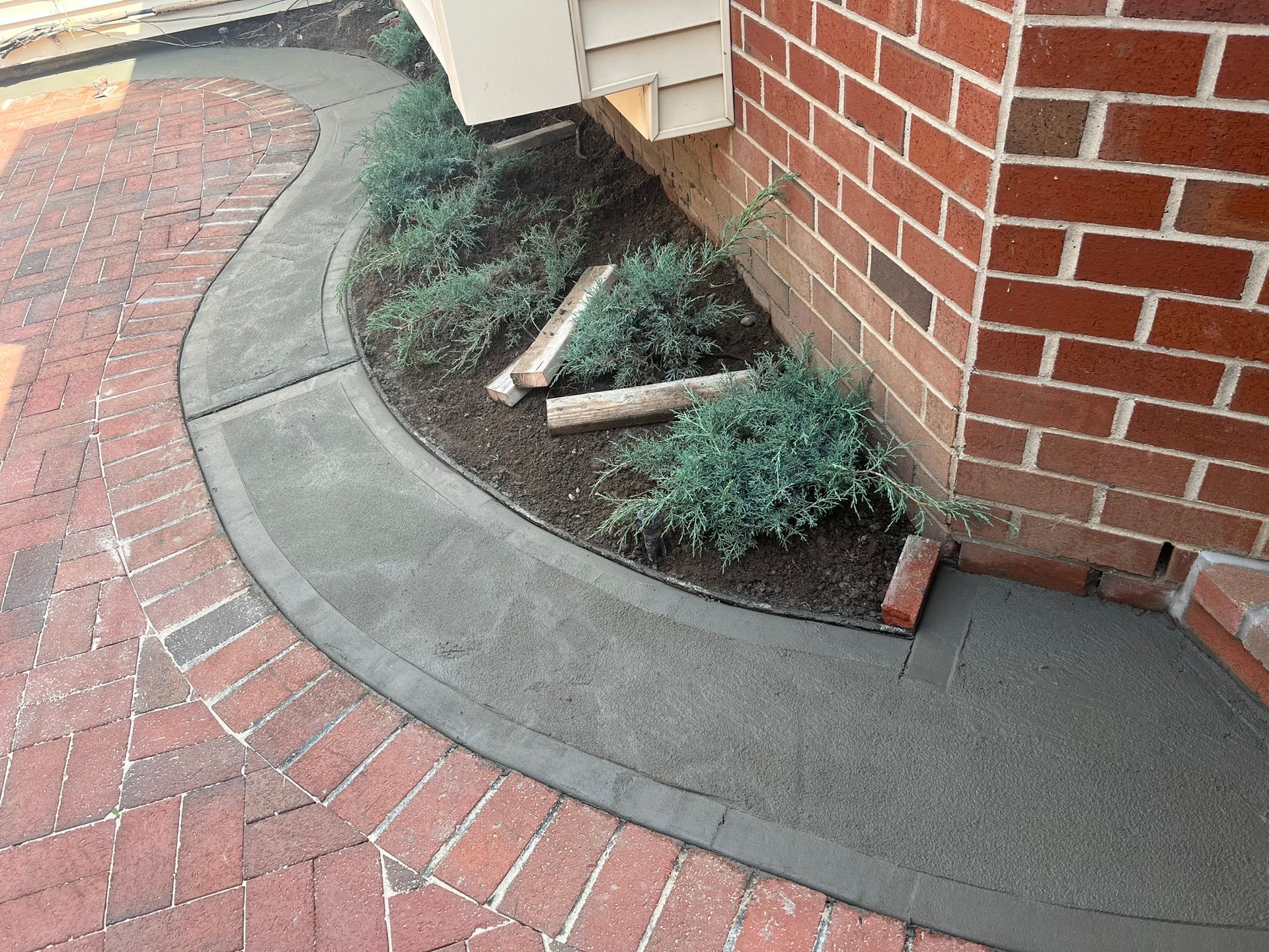 Curved brick walkway beside a brick wall with low shrubs and a small broken branch on the ground