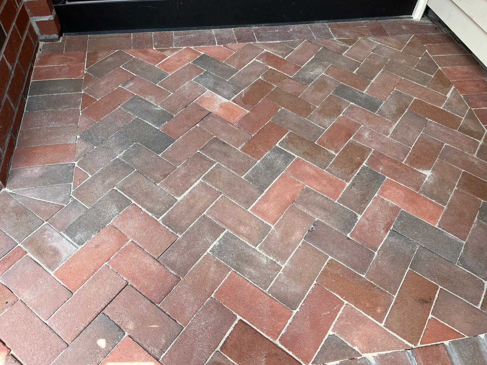 Brick herringbone walkway of red, gray, and tan pavers in front of a dark doorway