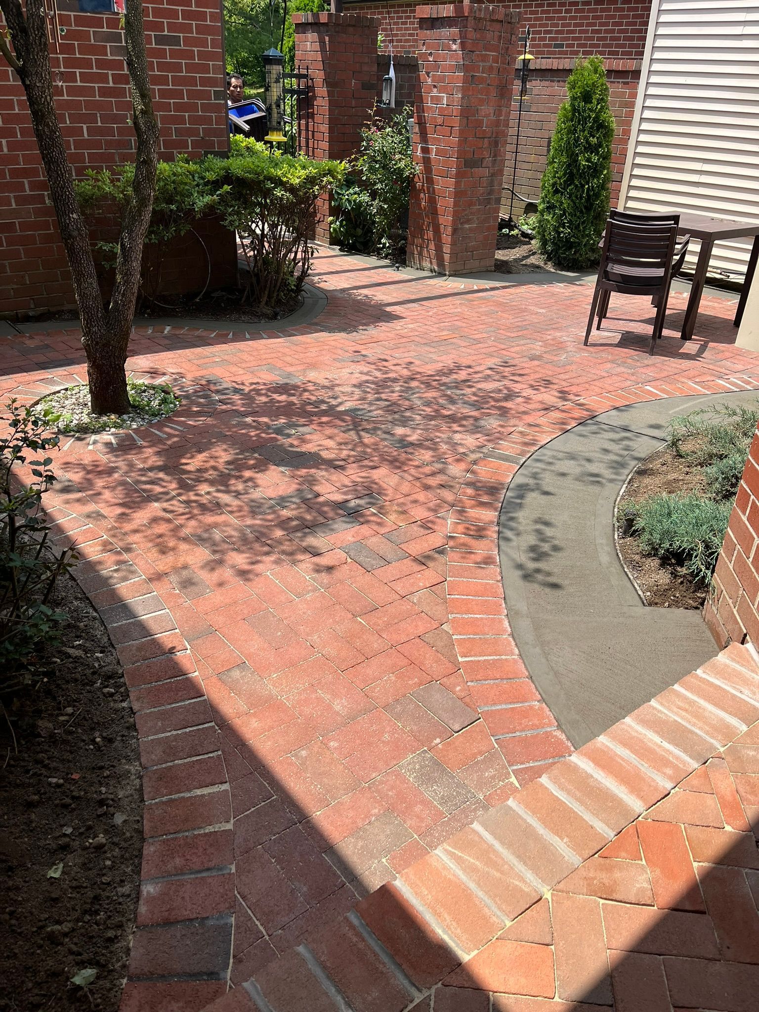 Brick courtyard with trees, shrubs, and a small seating area in front of a brick wall.